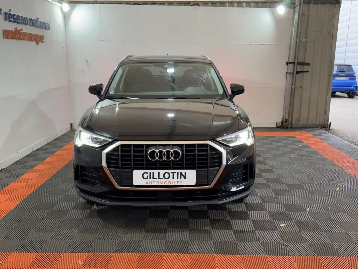 Audi Q3 noir vue de face en intérieur, avec calandre chromée et phares LED allumés.