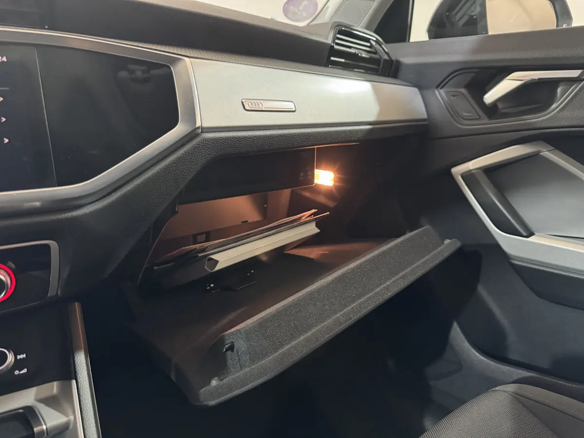 Vue intérieure côté passager de l'Audi Q3 35 TFSI 2022 noire, boîte à gants ouverte avec lumière intérieure allumée.