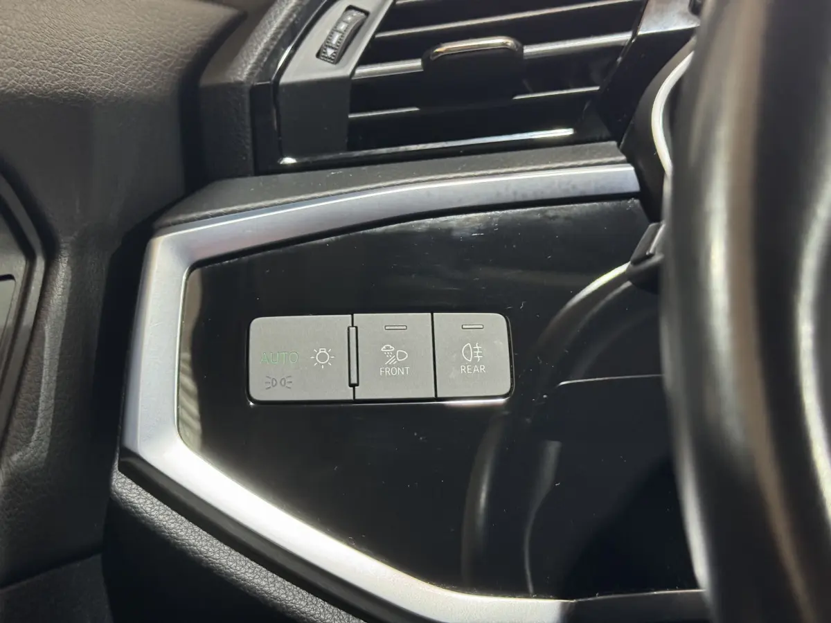 Détail des commandes d’éclairage sur panneau noir brillant côté gauche du volant d’un Audi Q3 noir 2022.