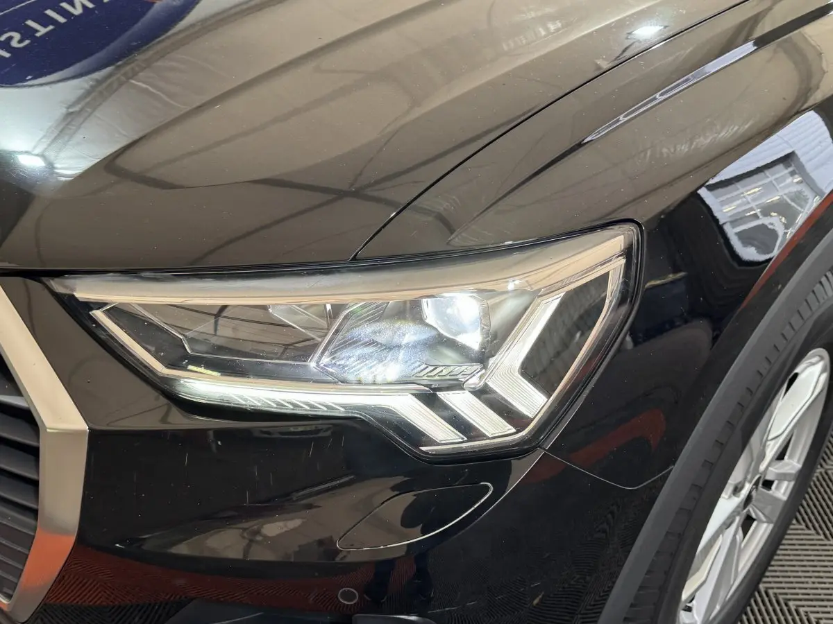 Gros plan sur le phare avant droit LED d’un Audi Q3 noir 2022, mettant en valeur ses lignes anguleuses et la jante alu visible.