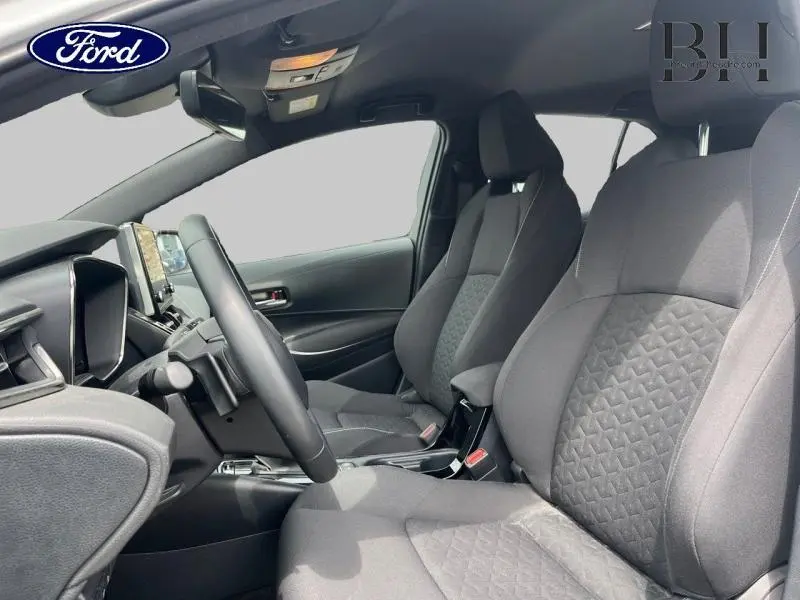 Vue intérieure côté conducteur de la Toyota Corolla 184h Dynamic Business 2022 avec sièges tissu noir et volant cuir multifonction.