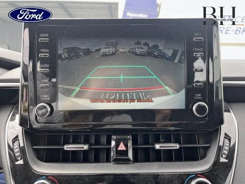 Écran tactile central montrant la caméra de recul d'une Toyota Corolla blanche, vue intérieure frontale.