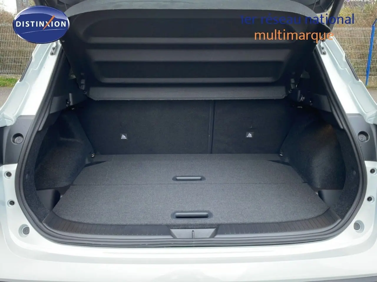 Coffre ouvert vu de l'arrière d'un Nissan Qashqai blanc nacré, plancher de coffre plat et espace de rangement spacieux.