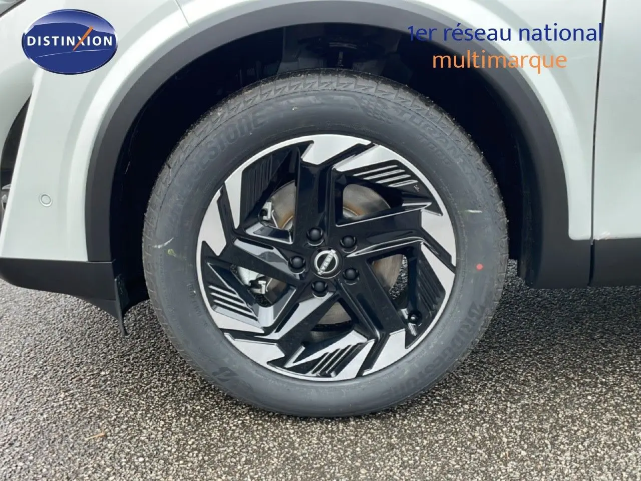 Gros plan sur la roue avant gauche du Nissan Qashqai blanc nacré, mettant en valeur la jante noire et argentée au design moderne.