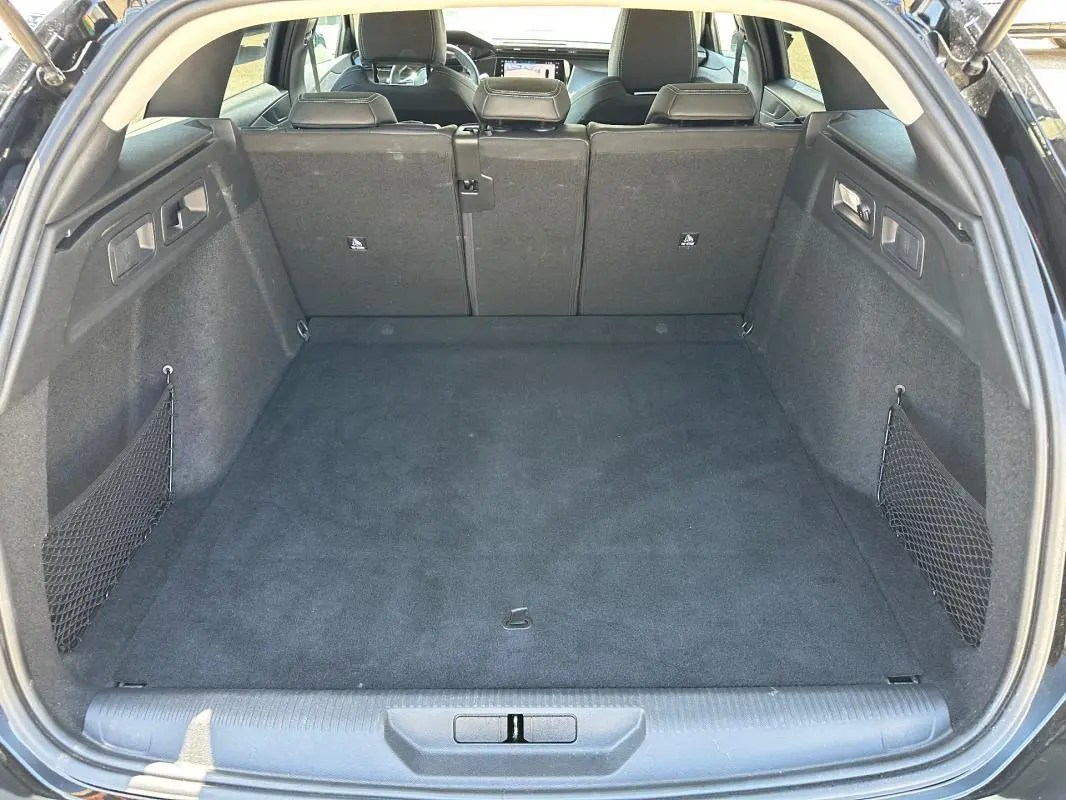 Coffre spacieux ouvert de la Peugeot 308 SW Hybrid 145 noir, avec sièges arrière en position relevée et filet de rangement latéral.