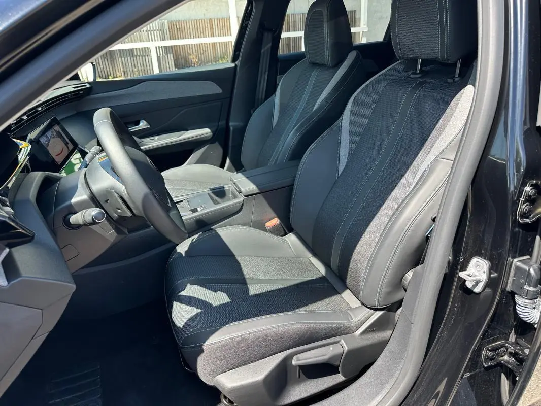 Vue intérieure côté conducteur de la Peugeot 308 SW Hybrid noire, mettant en valeur les sièges en tissu et cuir avec accoudoir central.