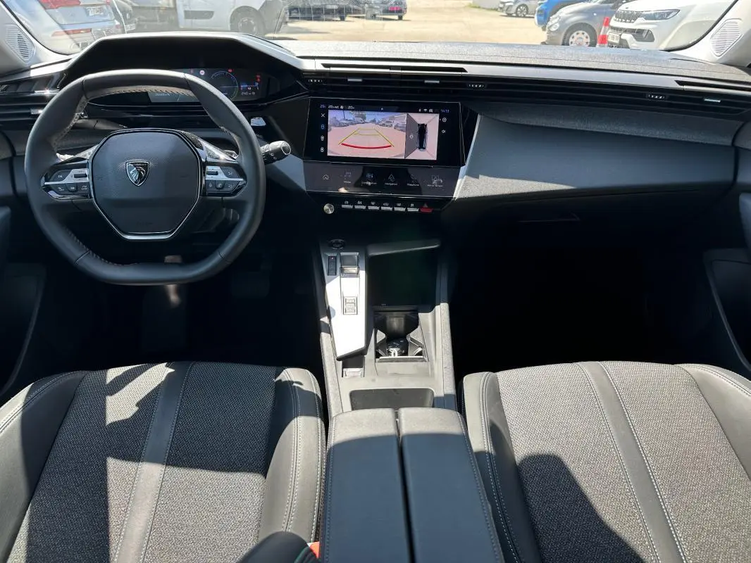 Intérieur noir de la Peugeot 308 SW Hybrid 2025, vue de face sur le volant, écran tactile et console centrale moderne.