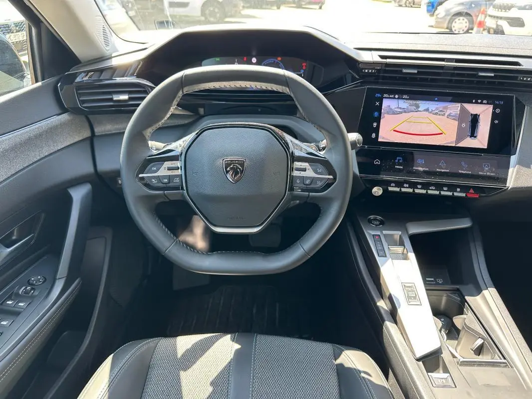 Vue intérieure frontale du poste de conduite noir du Peugeot 308 SW Hybrid avec volant multifonction et écran tactile de caméra de recul.