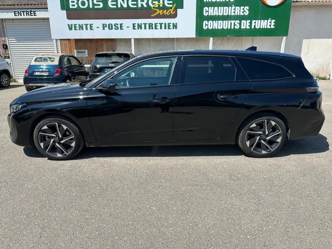 Profil latéral gauche d'une Peugeot 308 SW Hybrid noire 2025 avec jantes alliage 17 pouces, stationnée en extérieur.