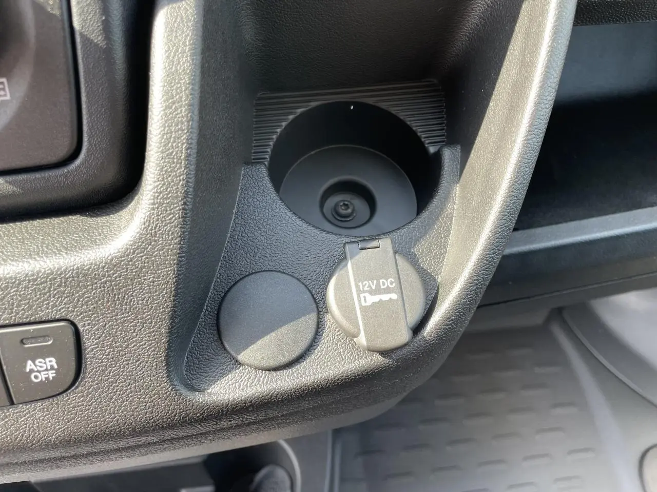 Gros plan sur la console centrale du Peugeot Boxer Fourgon blanc, montrant prise 12V et porte-gobelets.