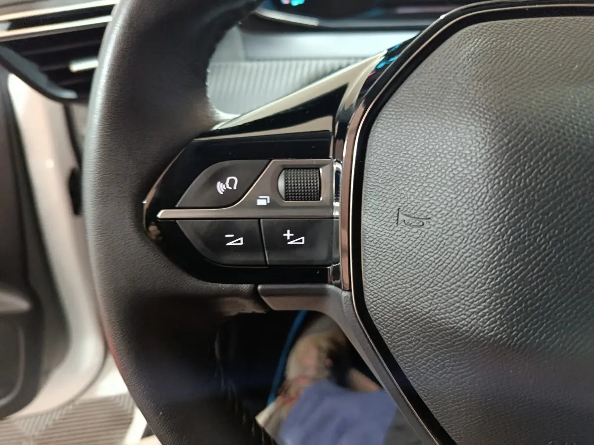 Gros plan sur les commandes gauche du volant cuir de la Peugeot 208 électrique blanche 2023 Active Pack.