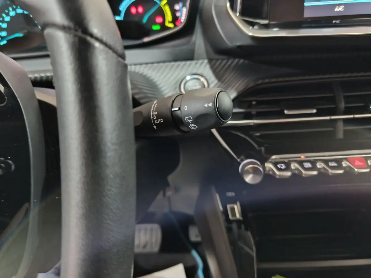 Vue rapprochée de l'intérieur de la Peugeot 208 électrique blanche, montrant le volant cuir et la commande d'essuie-glace.