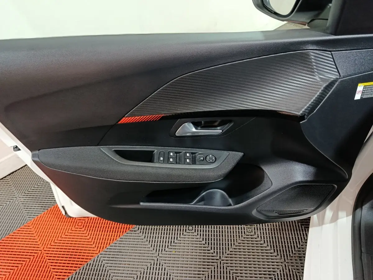 Porte intérieure côté gauche de Peugeot 208 électrique blanche 2023 avec insert carbone et bande rouge décorative.