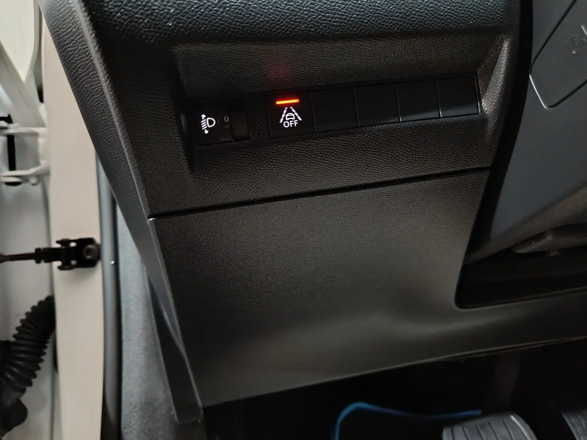 Gros plan sur les commandes d'assistance et réglage des phares côté gauche du tableau de bord noir d'une Peugeot 208 blanche électrique 2023.