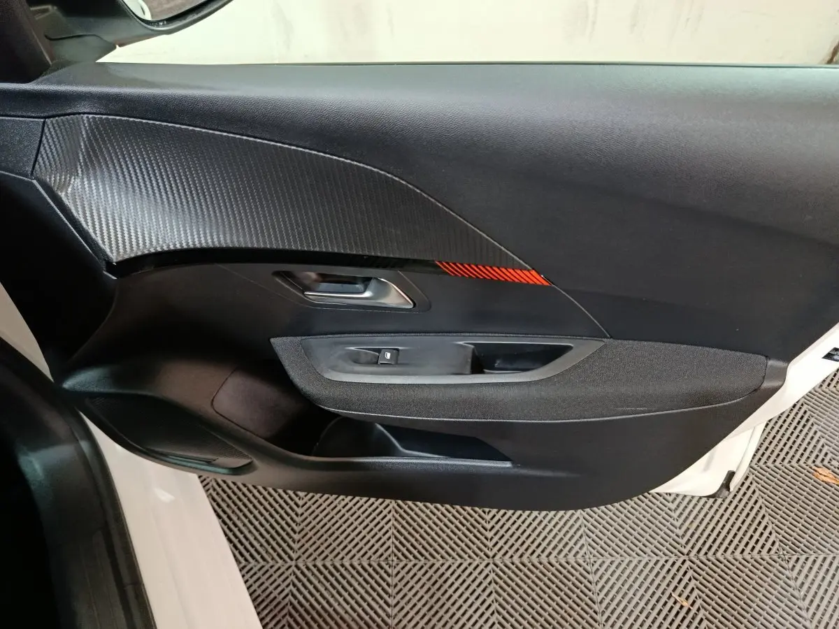 Vue rapprochée de la porte côté gauche d'une Peugeot 208 électrique blanche avec insert décoratif noir et rouge.