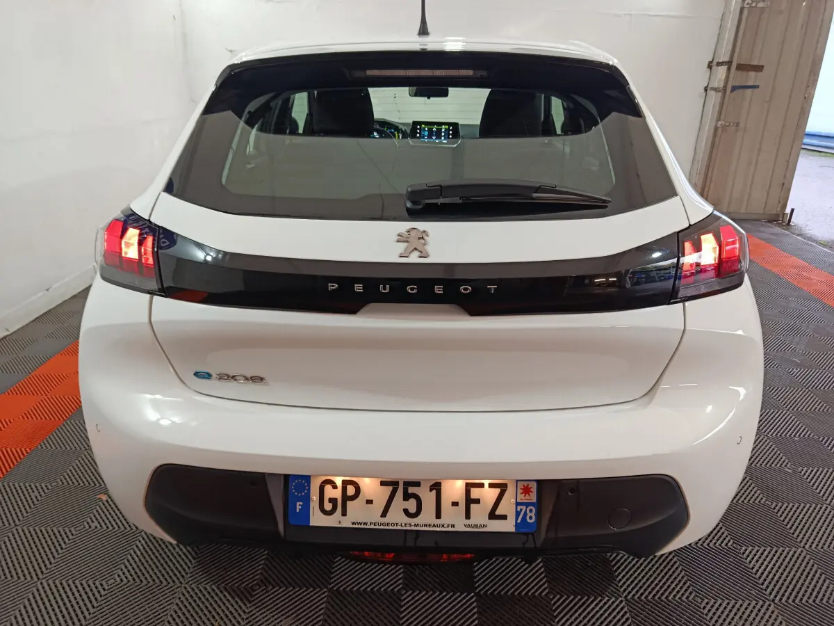 Vue arrière d'une Peugeot 208 électrique blanche de 2023 avec feux arrière LED allumés dans un garage.