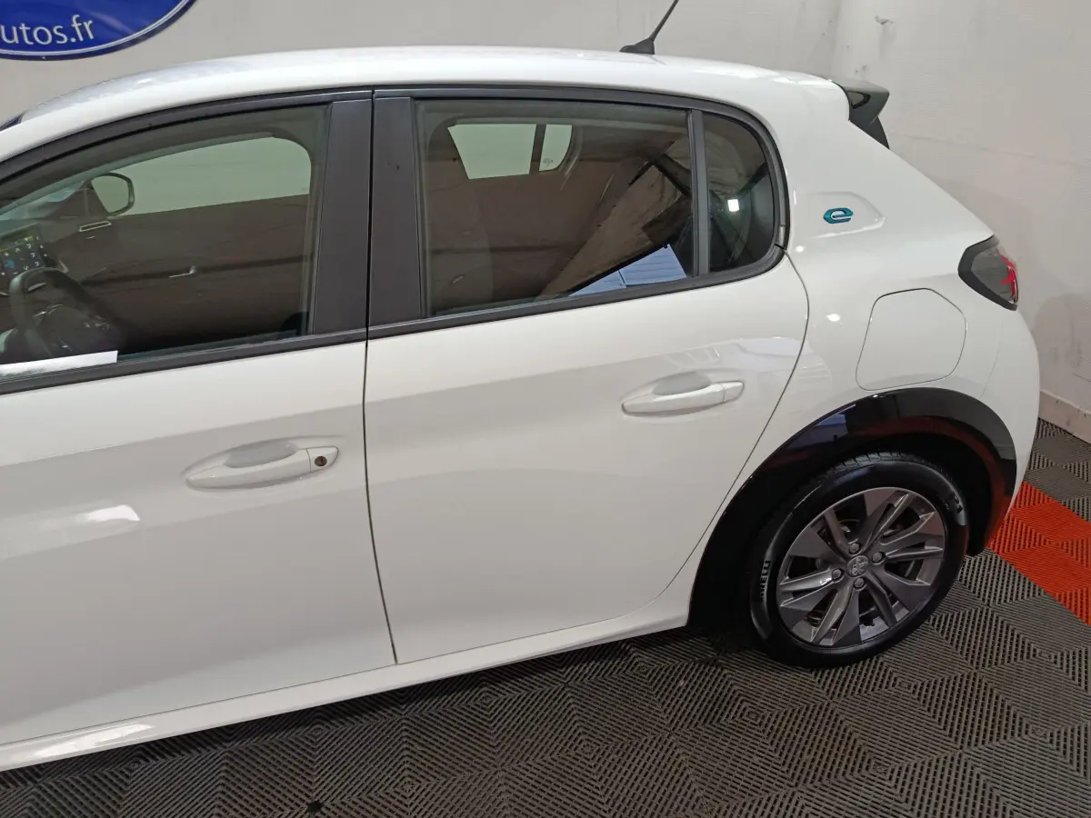Profil côté droit d'une Peugeot 208 électrique blanche 2023 avec logo "e" bleu sur l'aile arrière.