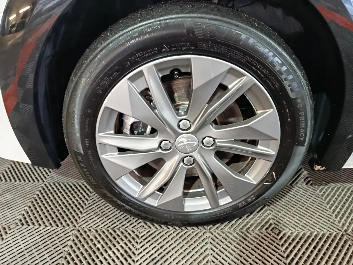 Gros plan sur la roue avant droite d'une Peugeot 208 électrique blanche, jante alliage et pneu Michelin visible.
