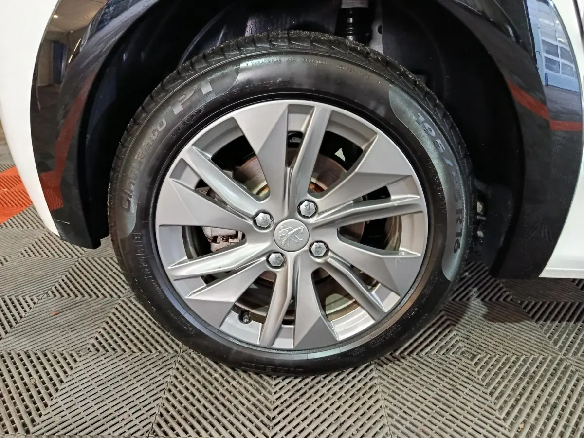 Gros plan sur la roue avant droite d'une Peugeot 208 électrique blanche, avec jante alliage argentée et logo lion central.