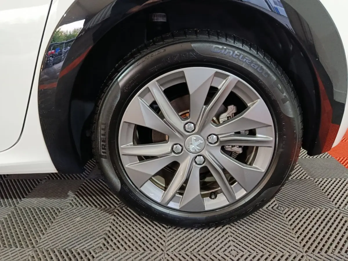 Gros plan sur la roue avant gauche blanche d'une Peugeot 208 électrique 2023 avec jante argentée et logo lion central.