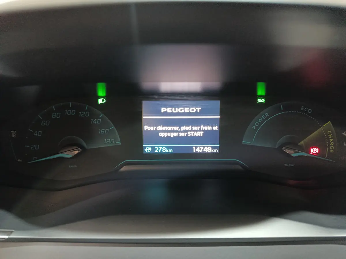 Tableau de bord numérique de Peugeot 208 électrique 2023, affichant l'autonomie et les voyants allumés.