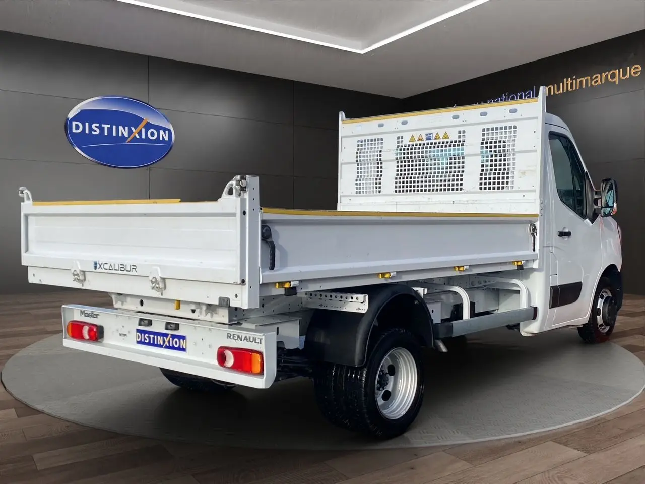 Vue 3/4 arrière droite d’un Renault Master blanc avec benne Excalibur, présenté en intérieur showroom.