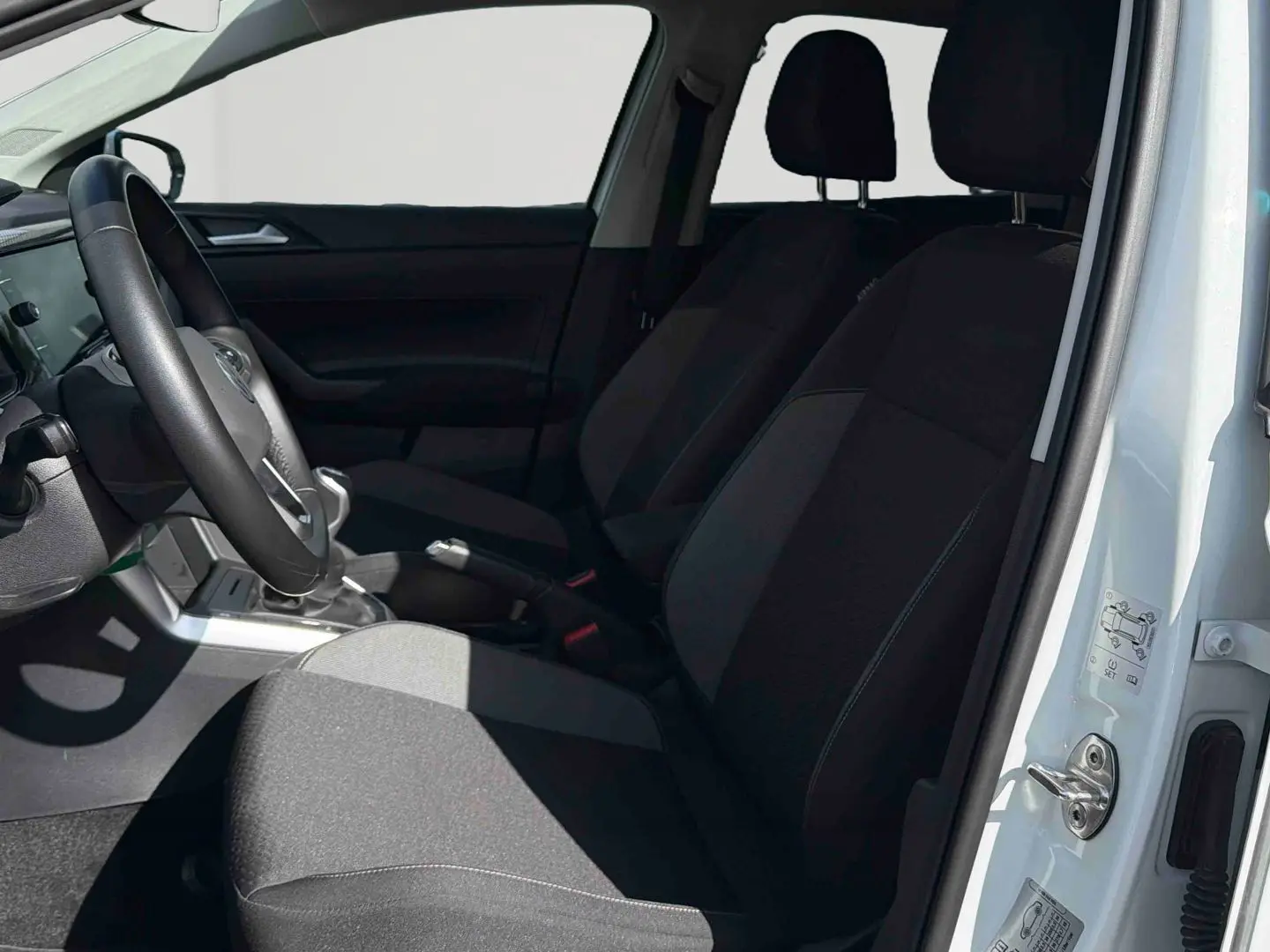 Intérieur avant côté conducteur d'une Volkswagen Polo blanche 2025, sièges noirs et volant cuir multifonctions visible.