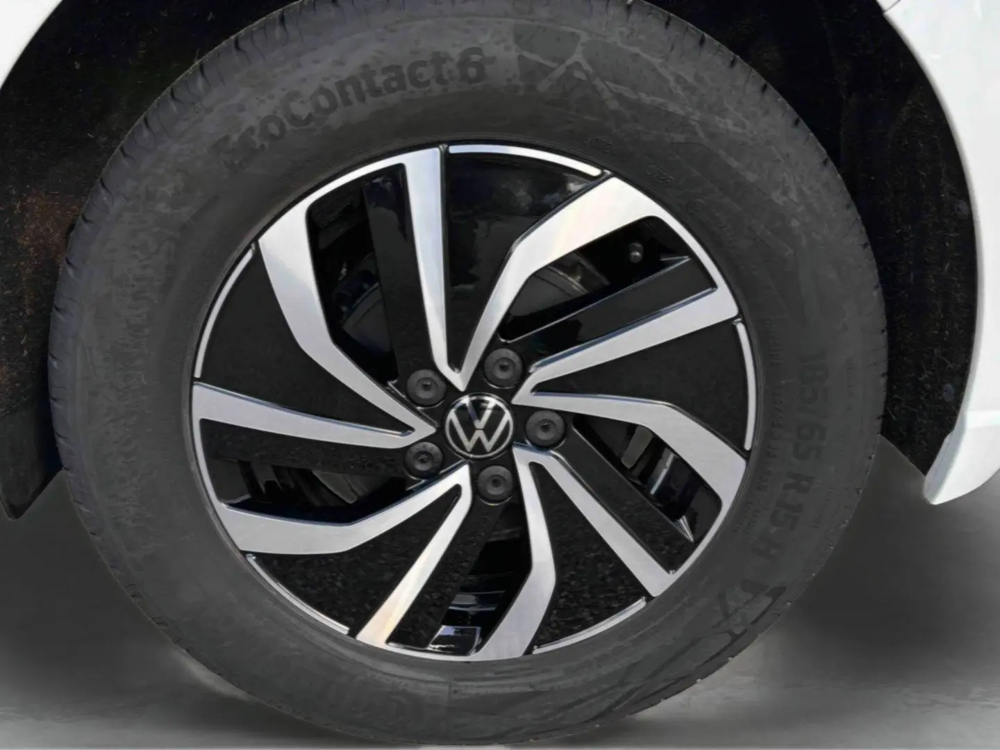 Gros plan sur la jante alliage 15 pouces bicolore noire et argentée d’une Volkswagen Polo blanche, pneu 185/65 R15 visible.