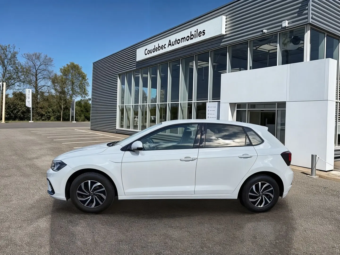 Vue de profil côté gauche d'une Volkswagen Polo blanche 2025 avec jantes alliage 15 pouces, stationnée devant un bâtiment.