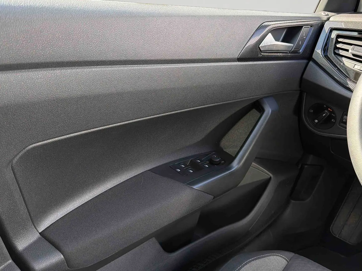 Détail de la porte avant gauche noire de la Volkswagen Polo 2025 avec commandes électriques des vitres et poignée intégrée.