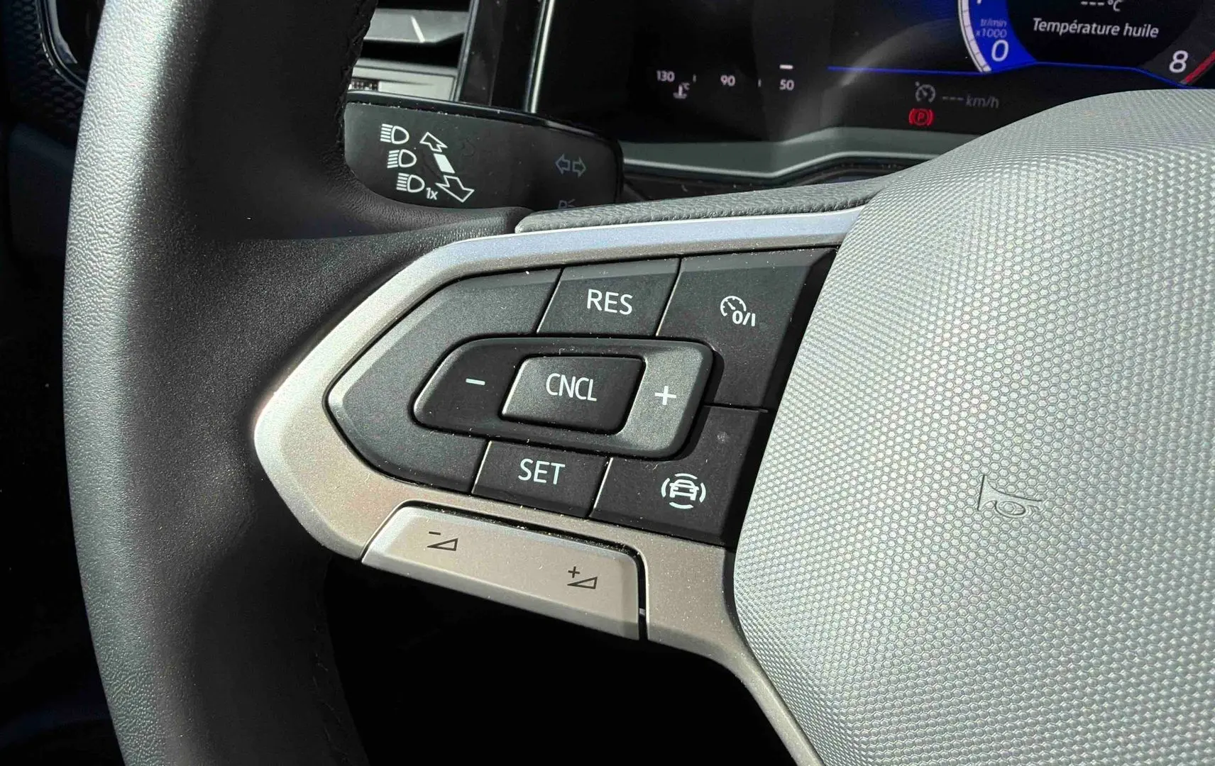 Gros plan sur les commandes du régulateur de vitesse au volant cuir gris d’une Volkswagen Polo blanche 2025.