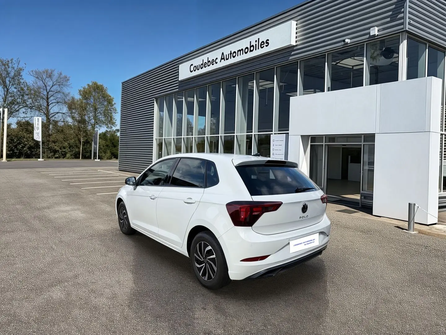 Vue 3/4 arrière droite d'une Volkswagen Polo blanche 2025 stationnée devant un concessionnaire Coudebec Automobiles.