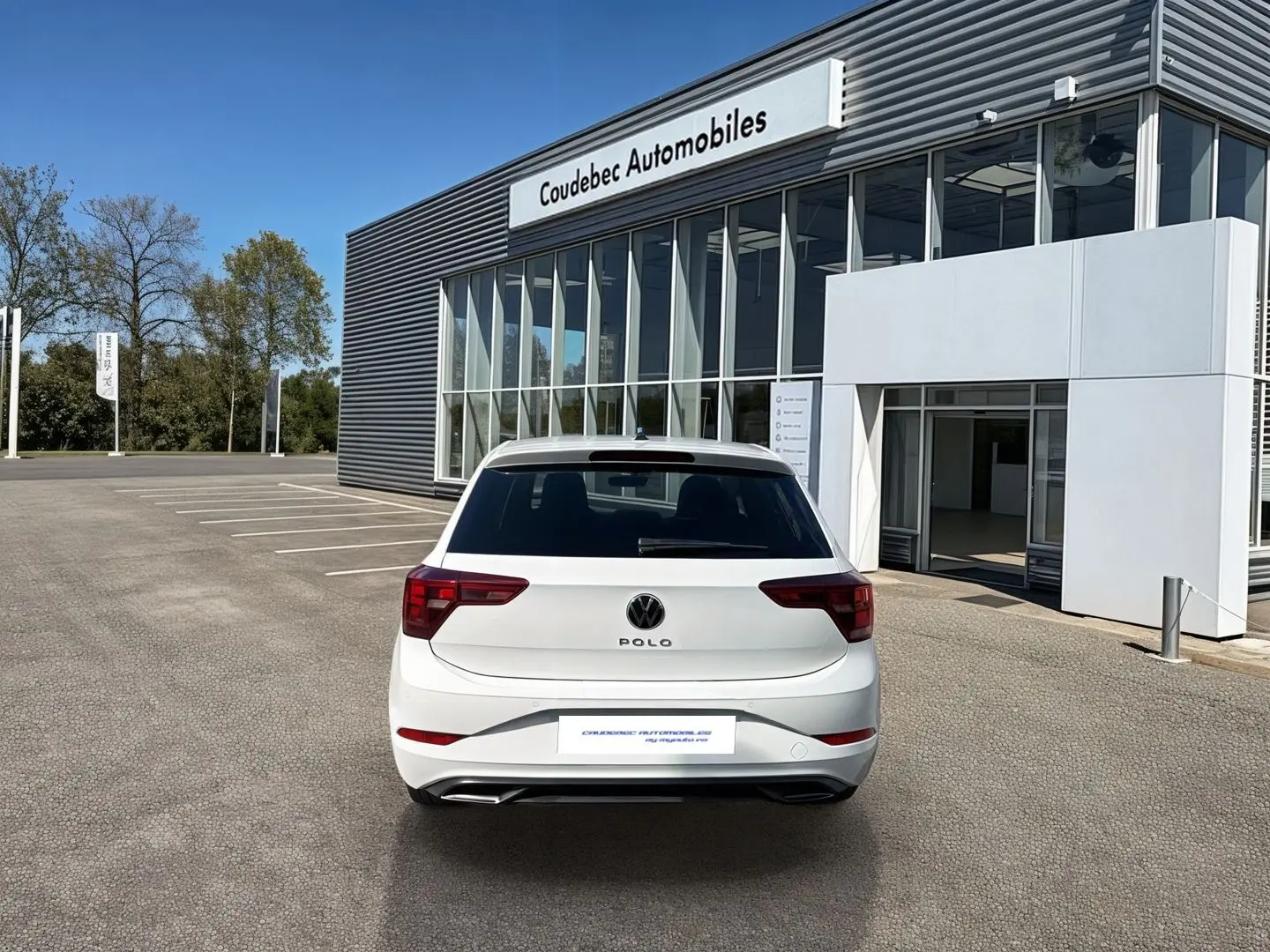 Vue arrière d'une Volkswagen Polo blanche 2025 stationnée devant un bâtiment moderne de concession automobile.
