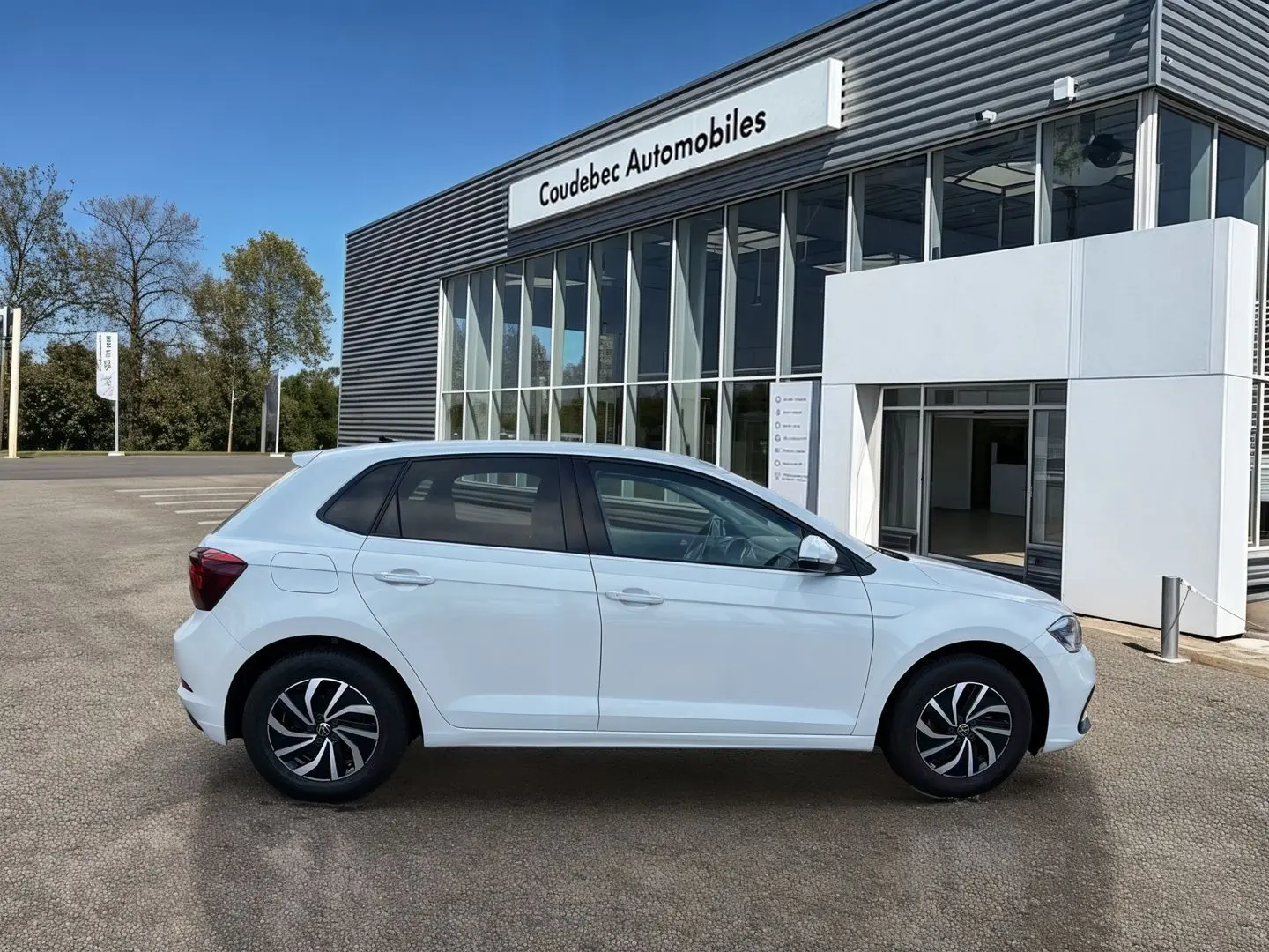 Volkswagen Polo blanche vue de profil côté gauche, garée devant un bâtiment moderne de concession.