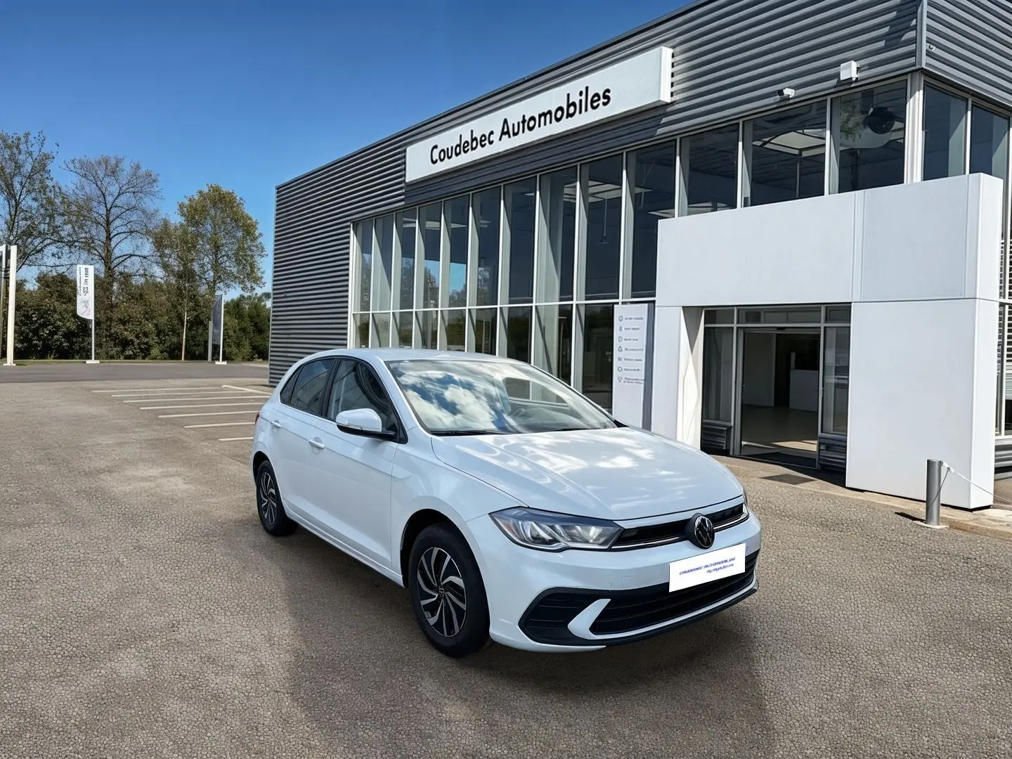 Volkswagen Polo blanche vue 3/4 avant droit devant un bâtiment de concession Coudebec Automobiles.