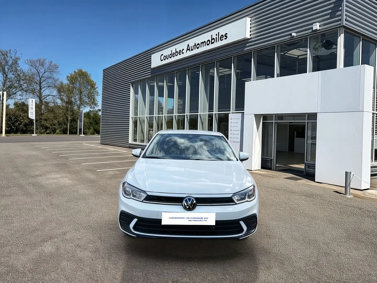 Volkswagen Polo blanche vue de face, avec calandre noire et feux LED, devant un bâtiment de concession automobile.