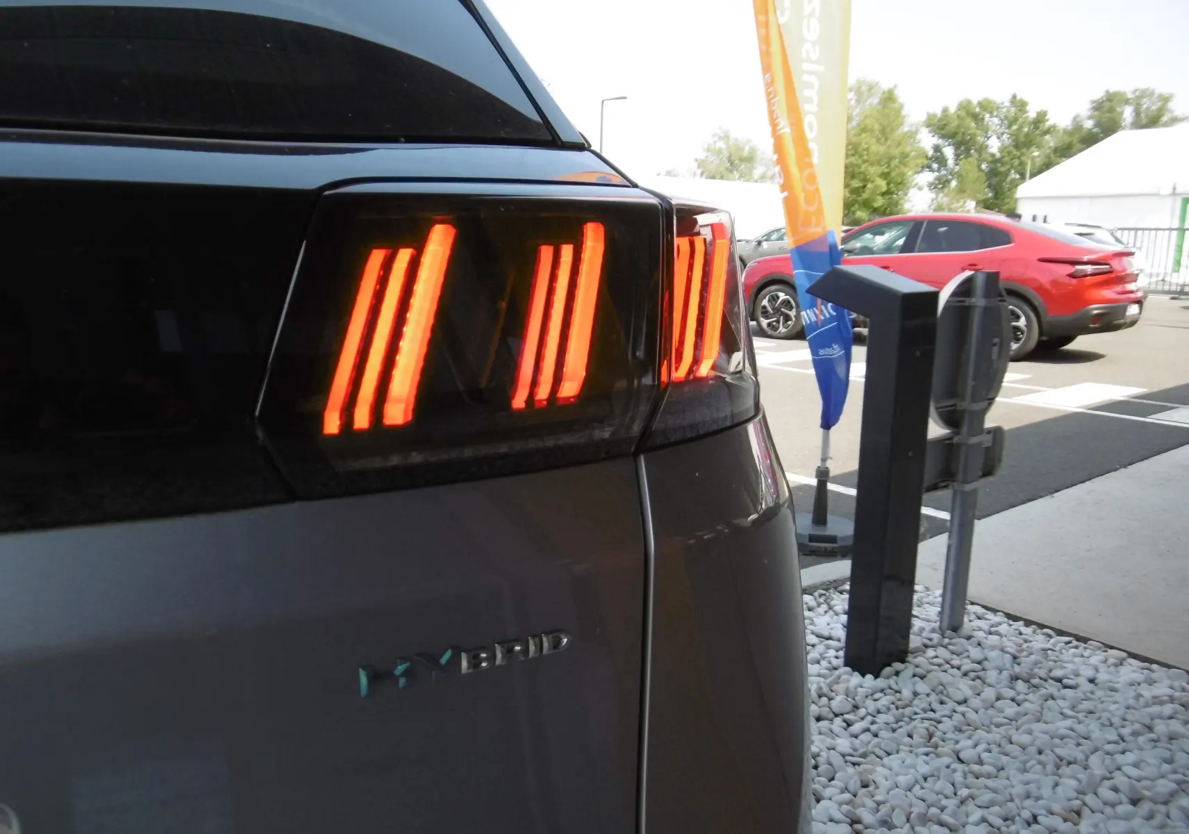 Gros plan sur le feu arrière droit allumé d'un Peugeot 3008 Hybrid gris Artense métal, avec le logo Hybrid visible.