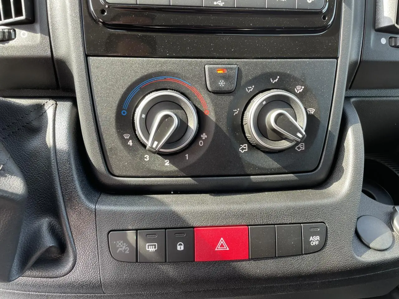 Gros plan sur les commandes de climatisation et les boutons de sécurité du tableau de bord du Peugeot Boxer Fourgon blanc.
