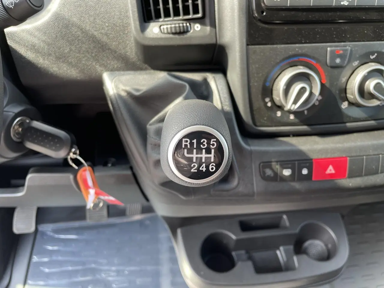 Gros plan sur le levier de vitesse manuel du Peugeot Boxer Fourgon blanc, avec commandes de climatisation et porte-gobelets visibles.