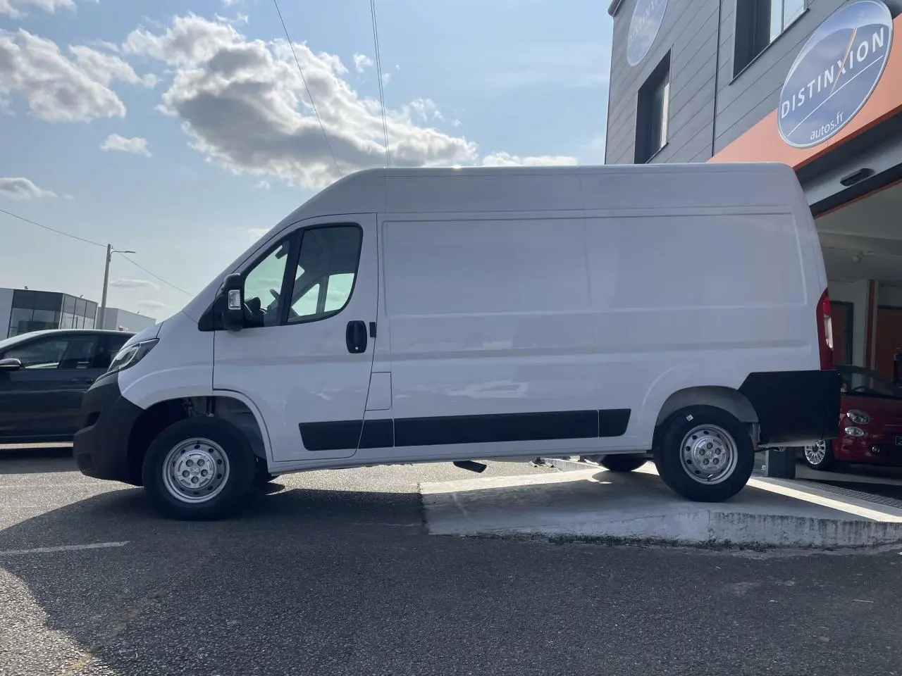 Profil droit du Peugeot Boxer Fourgon blanc 2023 avec porte latérale coulissante et protections noires sur parking.