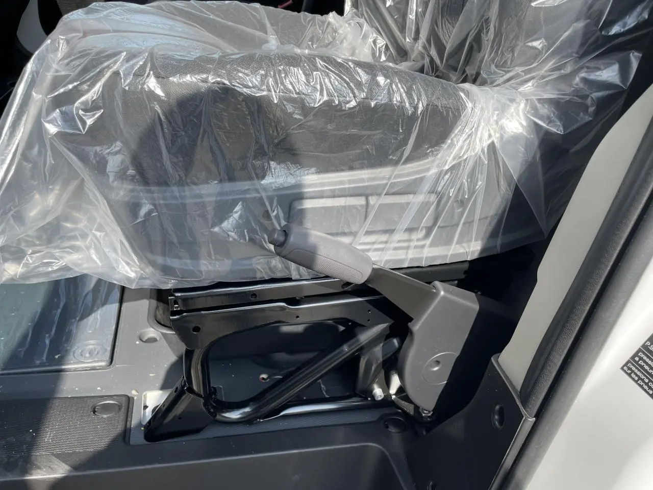 Détail du levier de frein à main noir sous un siège protégé par une housse plastique dans un Peugeot Boxer Fourgon blanc.