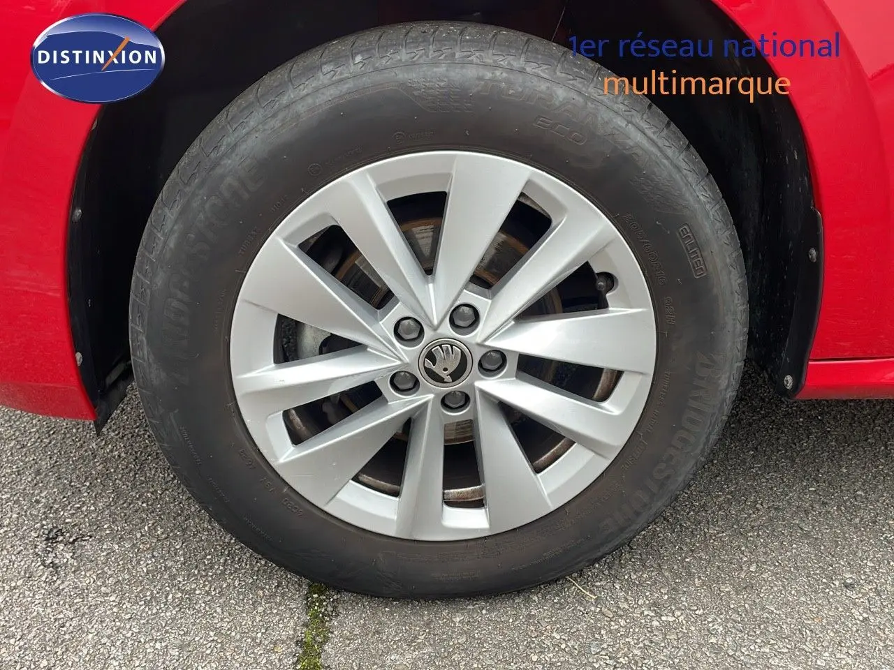 Gros plan sur la roue avant gauche d'un Skoda Kamiq rouge velvet metal avec jante alliage argentée.