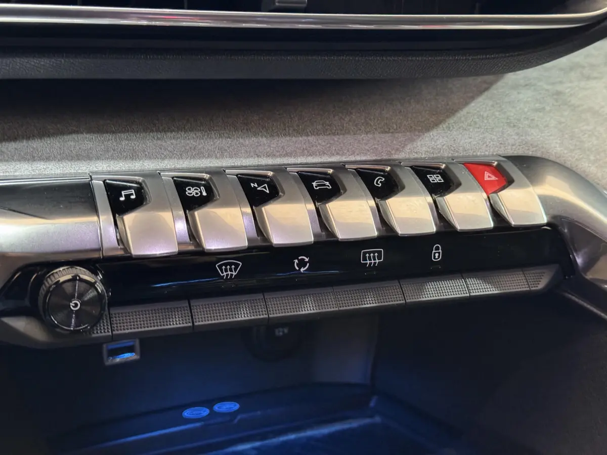 Gros plan sur la rangée de boutons argentés et noirs du tableau de bord du Peugeot 3008 GT gris clair, avec éclairage bleu dessous.