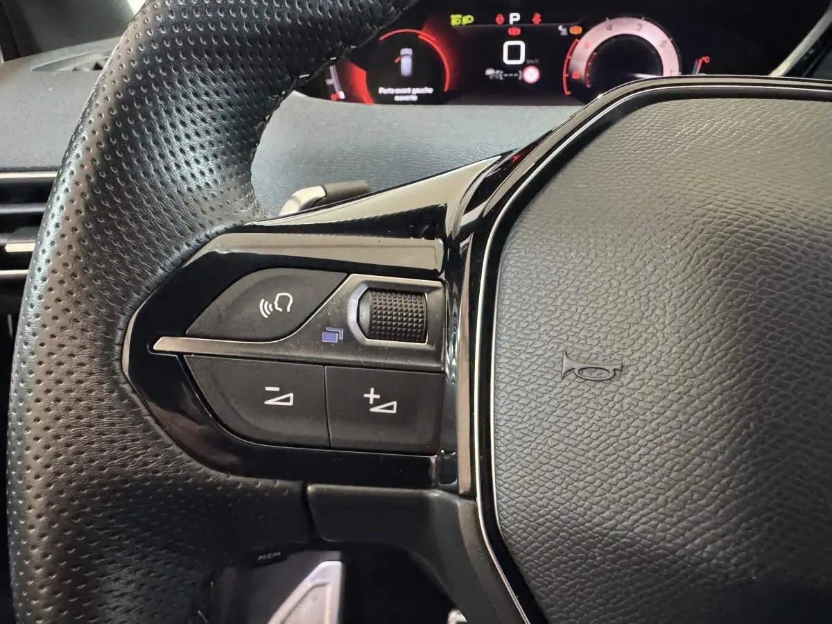 Gros plan sur le volant cuir noir perforé côté gauche du Peugeot 3008 2021 avec commandes audio et tableau de bord digital.