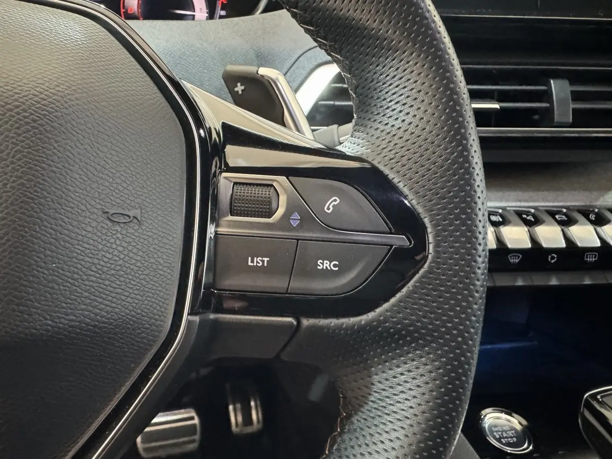 Gros plan sur le côté gauche du volant cuir perforé du Peugeot 3008 gris clair, avec commandes audio et tableau de bord en arrière-plan.