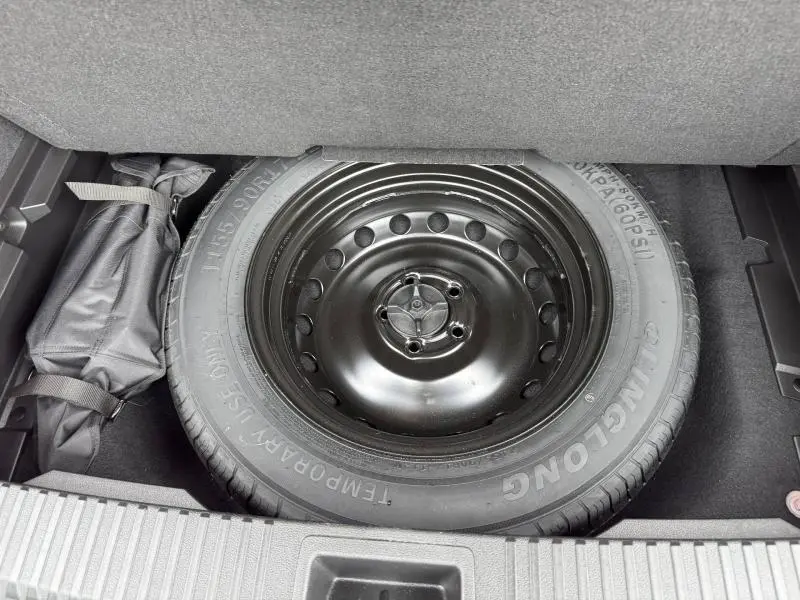 Roue de secours noire en vue plongeante dans le coffre d'un Renault Austral 2024, entourée de rangements gris.