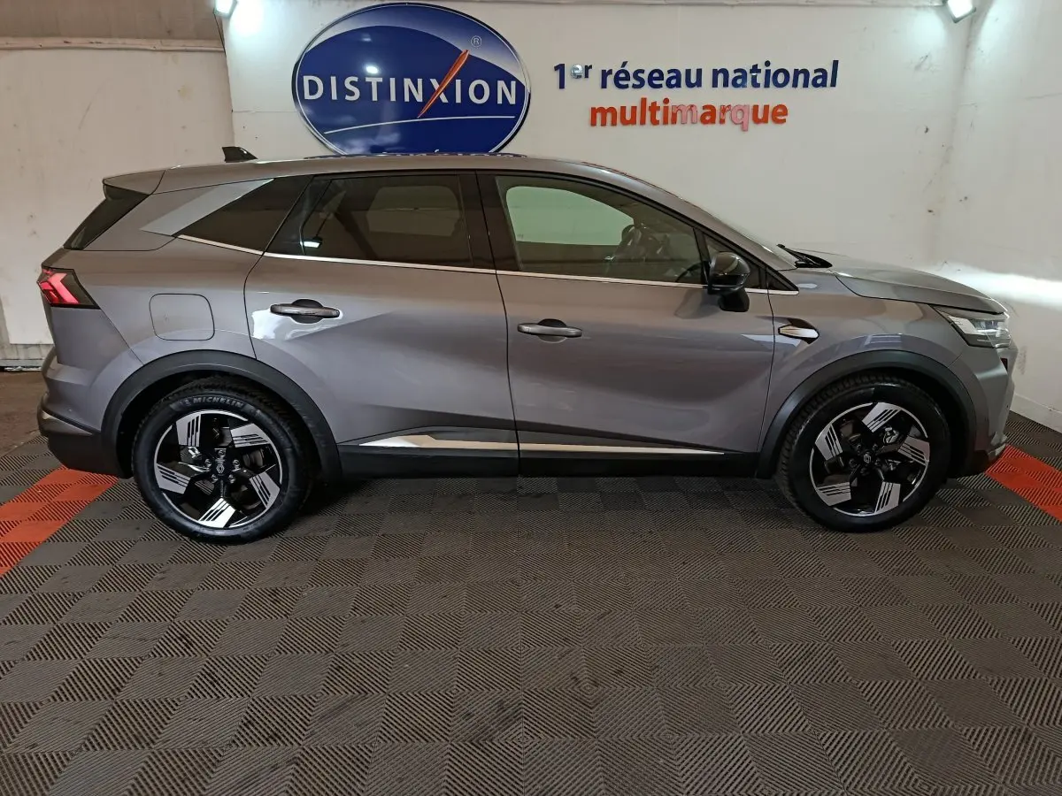 Vue de profil côté gauche d’un Renault SYMBIOZ gris avec jantes noires et détails chromés, en intérieur showroom.
