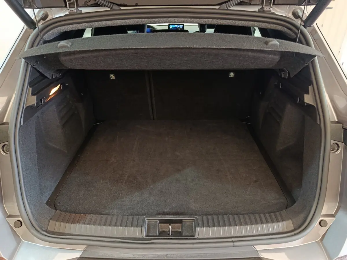 Coffre ouvert vu de l'arrière d'une Renault SYMBIOZ hybride 2025 couleur gris clair, avec tapis noir et éclairage intérieur.