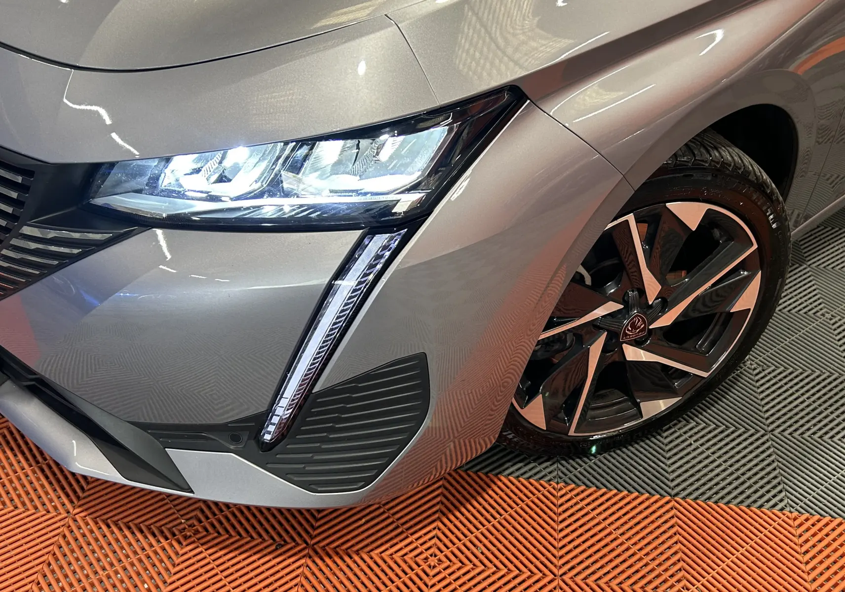 Gros plan sur l'avant droit gris métallisé de la Peugeot 308 2022 avec phare LED allumé et jante alliage distinctive.