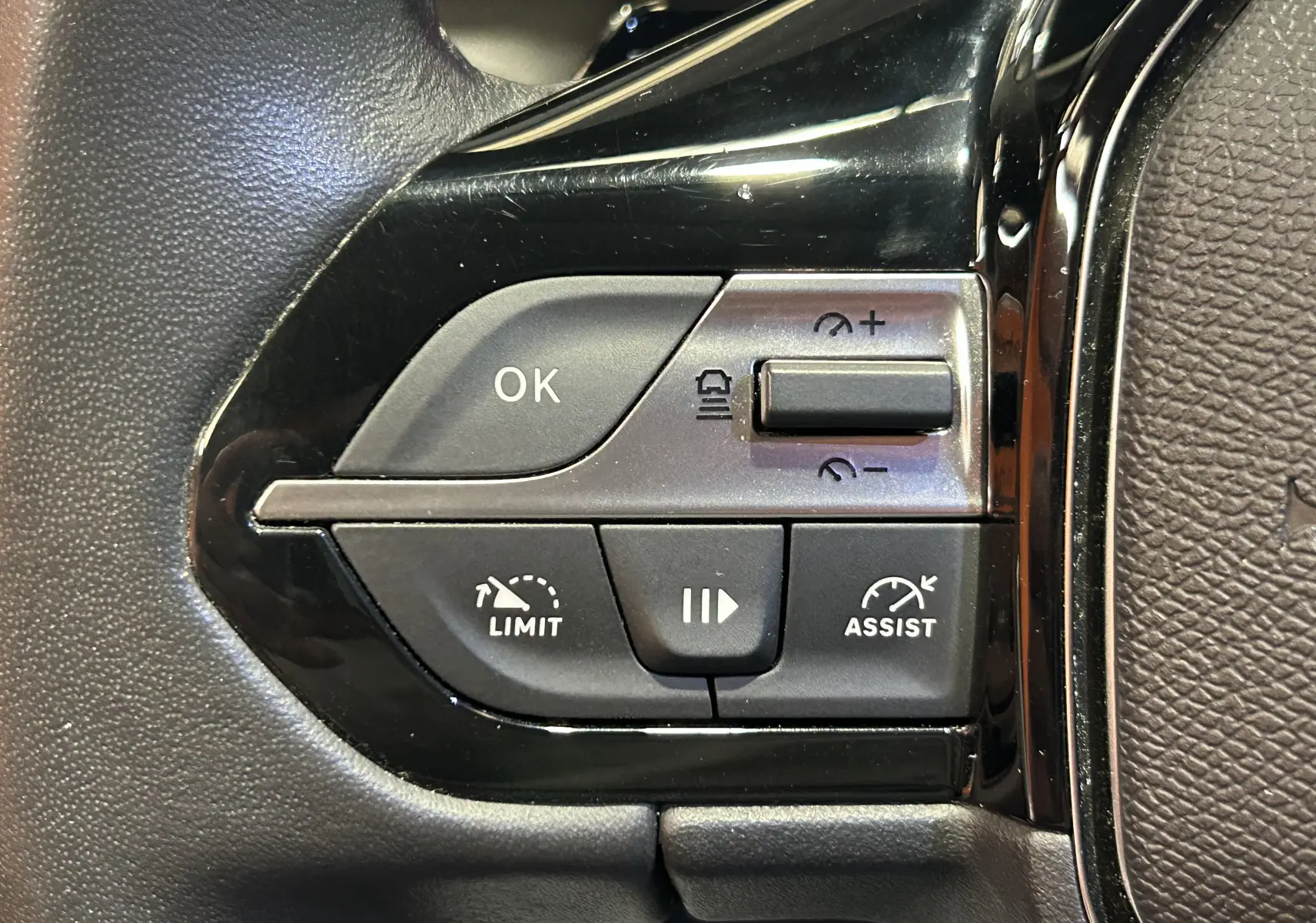 Gros plan sur les commandes noires du volant côté gauche de la Peugeot 308 gris, avec boutons de régulateur et limiteur de vitesse.